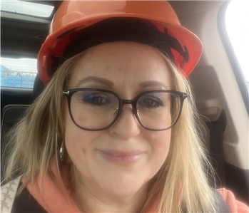 Blonde woman with large framed glasses wearing a hard hat and a smile